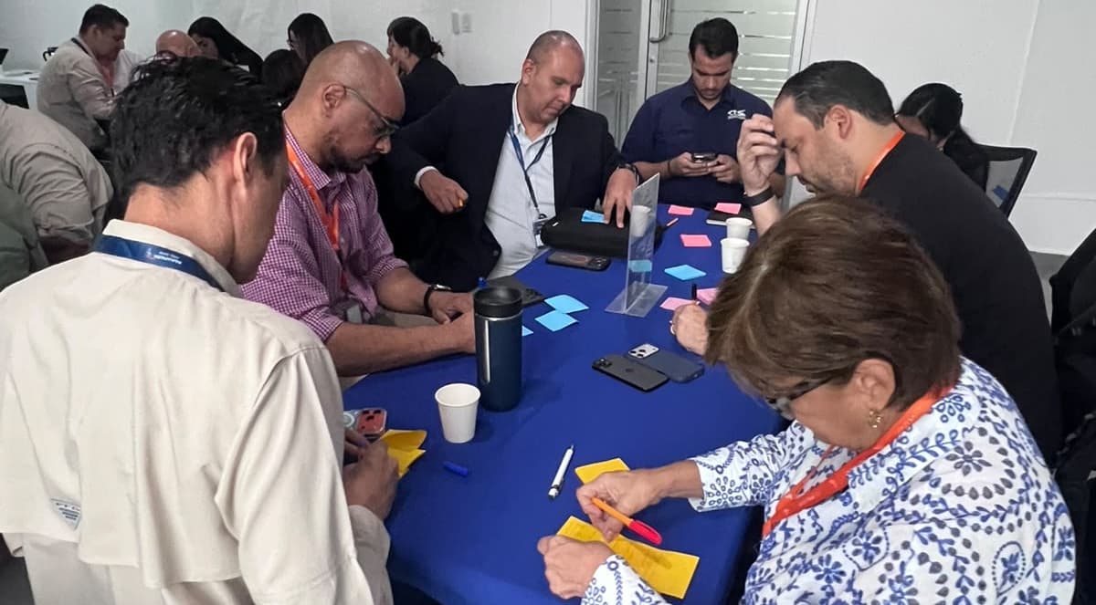 Miembros de un gremio trabajando con notas adhesivas alrededor de una mesa en un taller de co-creación